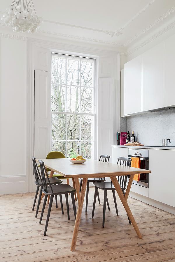 Simple White Fitted Kitchen In Renovated Period Building With Floor-to-ceiling Lattice Window, Stripped Wooden Floor And Retro Dining Set Photograph by Simon Maxwell Photography
