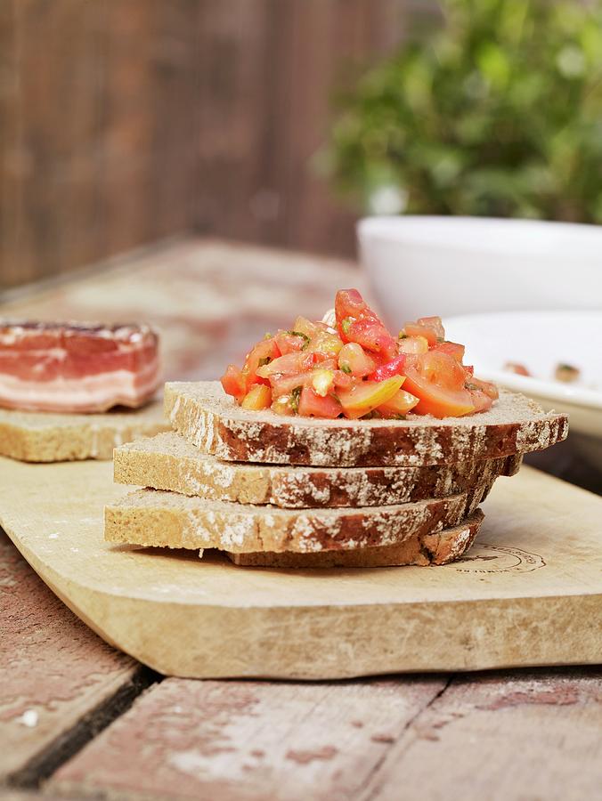 Slices Of Moist Rye Bread Stacked On A Chopping Board And Topped With Tomato Salad Photograph by Till Melchior