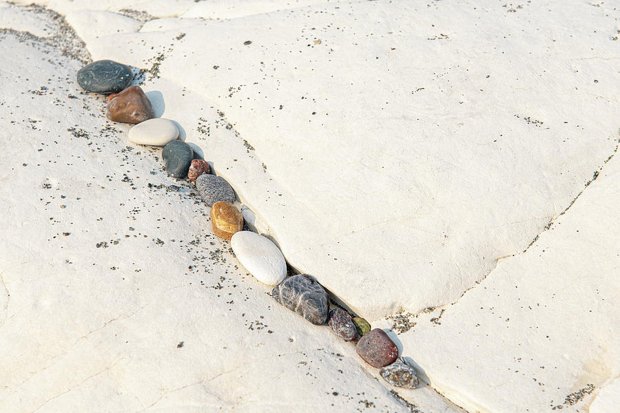 Small beach pebbles in a row on a rocky white surface. Photograph by Michalakis Ppalis