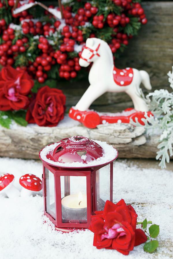 Small Candle Lantern And Rose In Artificial Snow In Front Of Rocking Horse Ornament And Winter Berries Photograph by Angelica Linnhoff