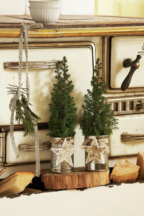 Small Fir Trees In Tin Cans Decorated With Christmas Baubles On Wooden Board In Front Of Vintage Kitchen Cooker Photograph by Heidi Frhlich