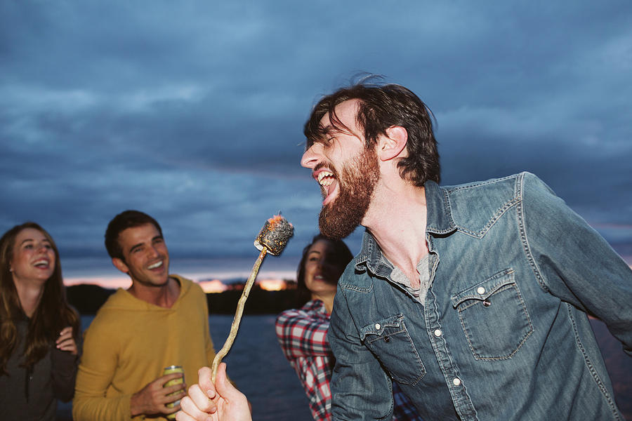 Portland Photograph - Smiling Friends Looking At Man Singing While Holding Roasted Marshmallow On Stick Against Cloudy Sky by Cavan Images