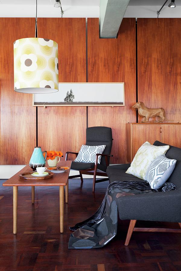 Sofa And Armchair With Grey Upholstery Around Simple Wooden Coffee Table Below Pendant Lamp With Retro-patterned Lampshade; Fitted Wooden Cupboards In Background Photograph by Great Stock!