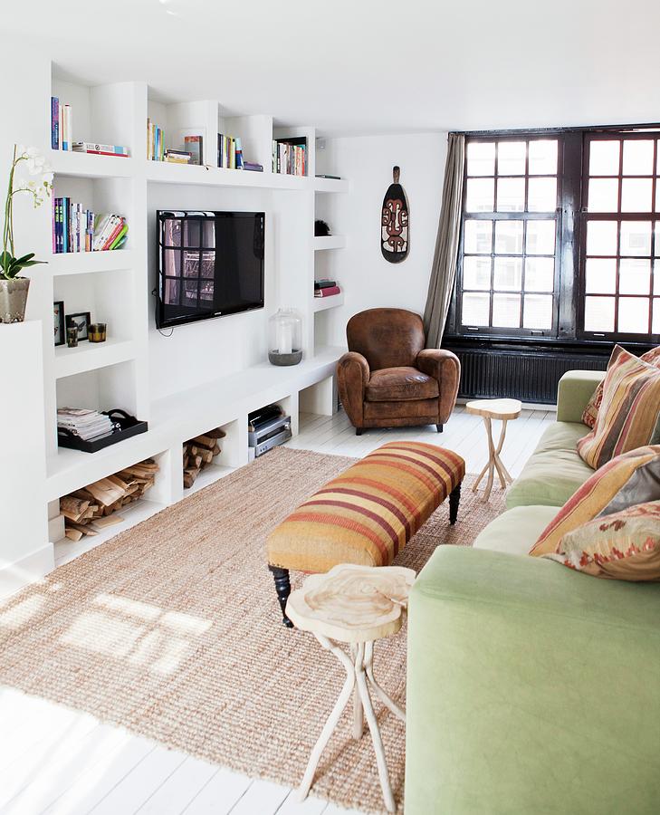 Sofa With Scatter Cushions And Ottoman Opposite Wall With Masonry Shelving And Wall-mounted Tv; Leather Armchair In Background Next To Black, Latticed French Doors Photograph by Barbara De Hosson
