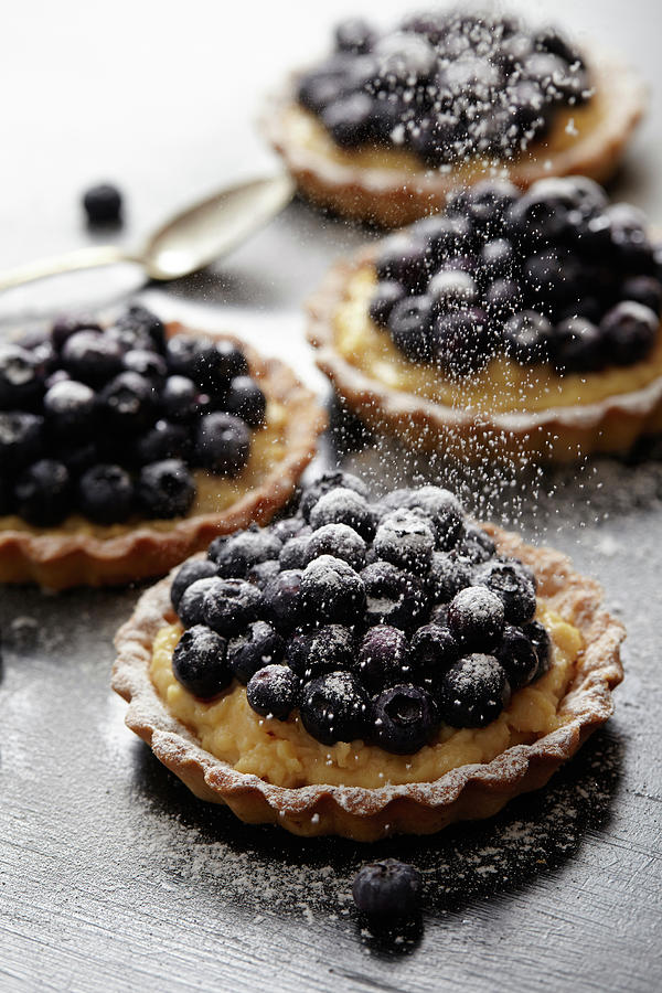 Sprinkling Ice Sugar Onto The Confectioners Custard And Blackcurrant Tartlets Photograph by Lukam