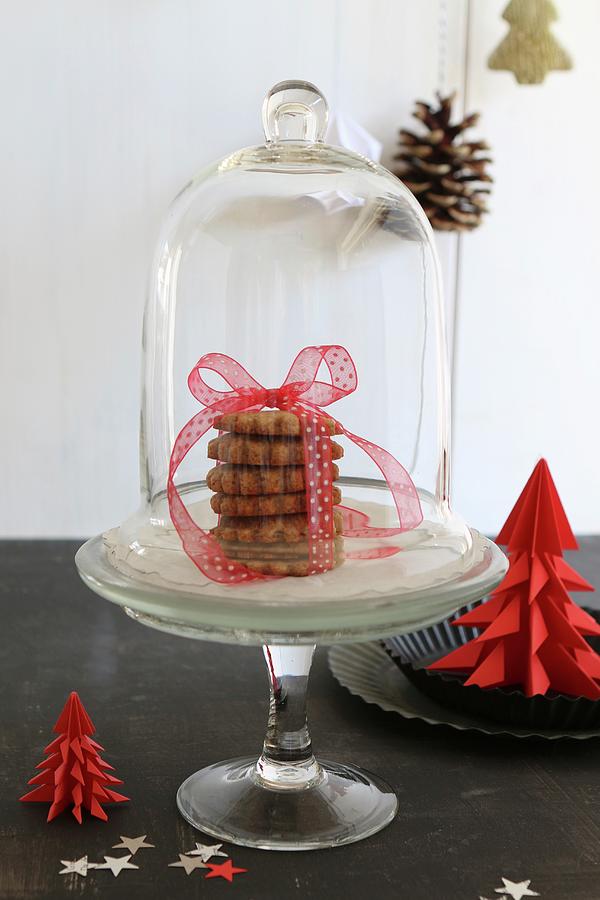 Stack Of Christmas Biscuits Tied With Ribbon Under Glass Cover Next To Red Paper Christmas Tree Photograph by Regina Hippel