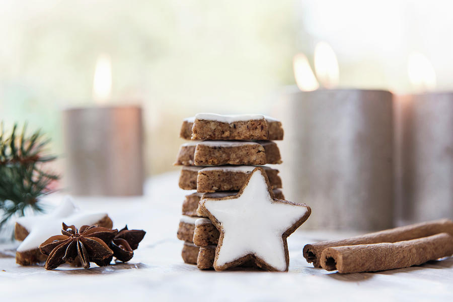 Stack Of Cinnamon Star Biscuits, Cinnamon Sticks, Star Anise And Lit Candles In Background Photograph by Jelena Filipinski