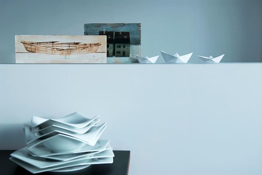 Stack Of Polygonal Plates Below Paper Boats And Nordic Painting Arranged On Half-height Wall Photograph by Matteo Manduzio