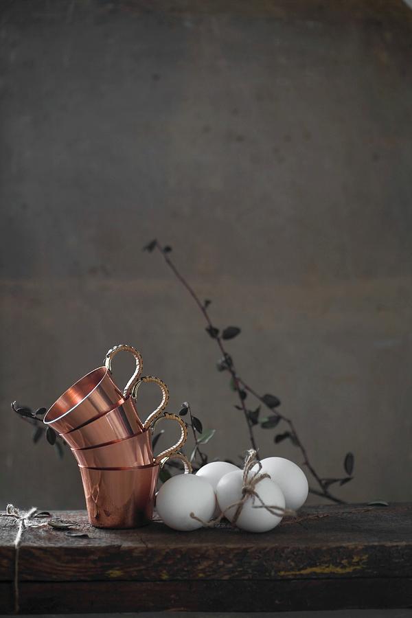Stacked Copper Cups And White Hens Eggs On Wooden Table Photograph by Alicja Koll
