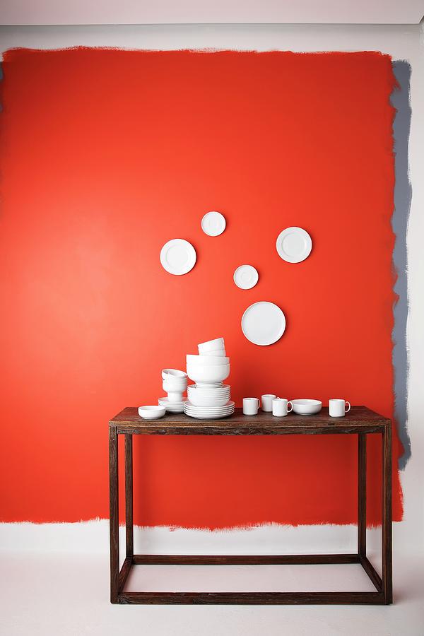 Stacks Of White China Crockery On Wooden Table Below Plates Hung On Red Wall Photograph by Roberto Rabe