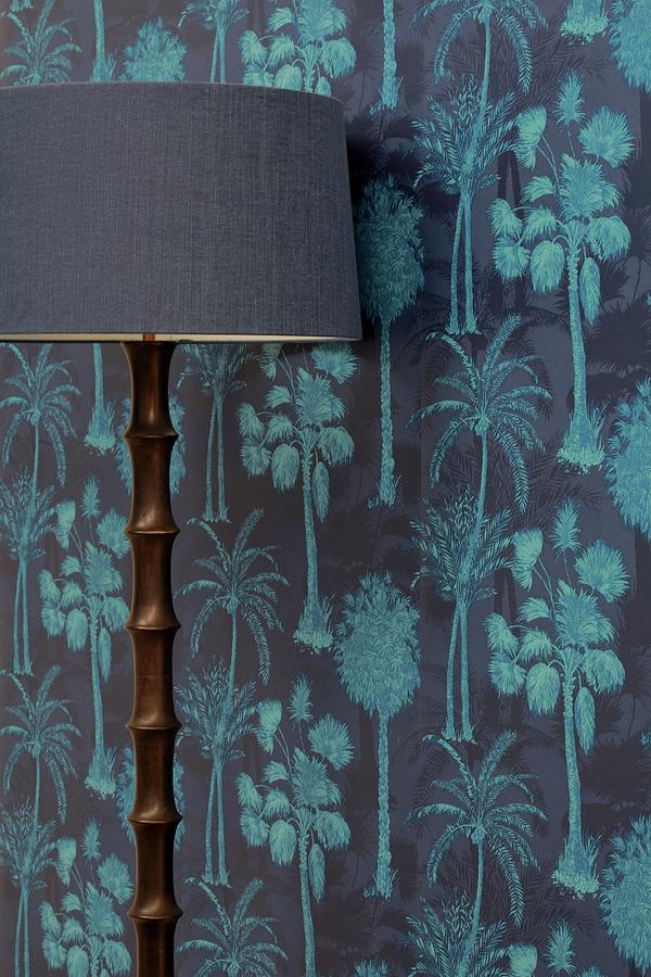 Standard Lamp With Wooden Base Against Wallpaper In Shades Of Blue With Pattern Of Coconut Palms Photograph by Great Stock!