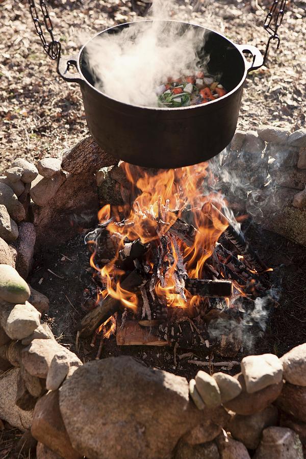 Steaming Vegetable Stew In Cooking Pot Suspended Over Campfire In Stone Hearth Photograph by Annette Nordstrom