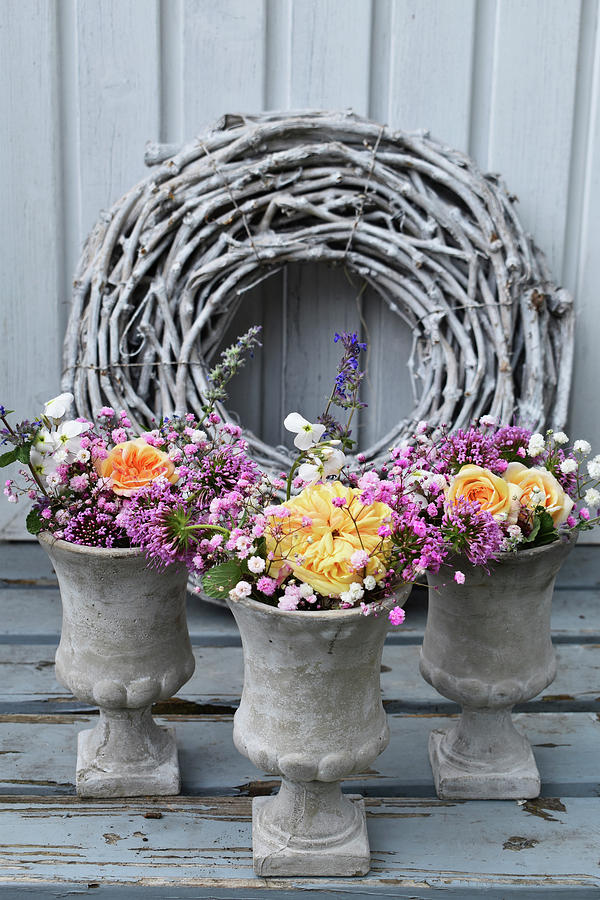 Summer Bouquets Of Roses, Caucasian Crosswort And Gypsophila In Small Concrete Urns In Front Of Wreath Of White-painted Vines Photograph by Susan Haag