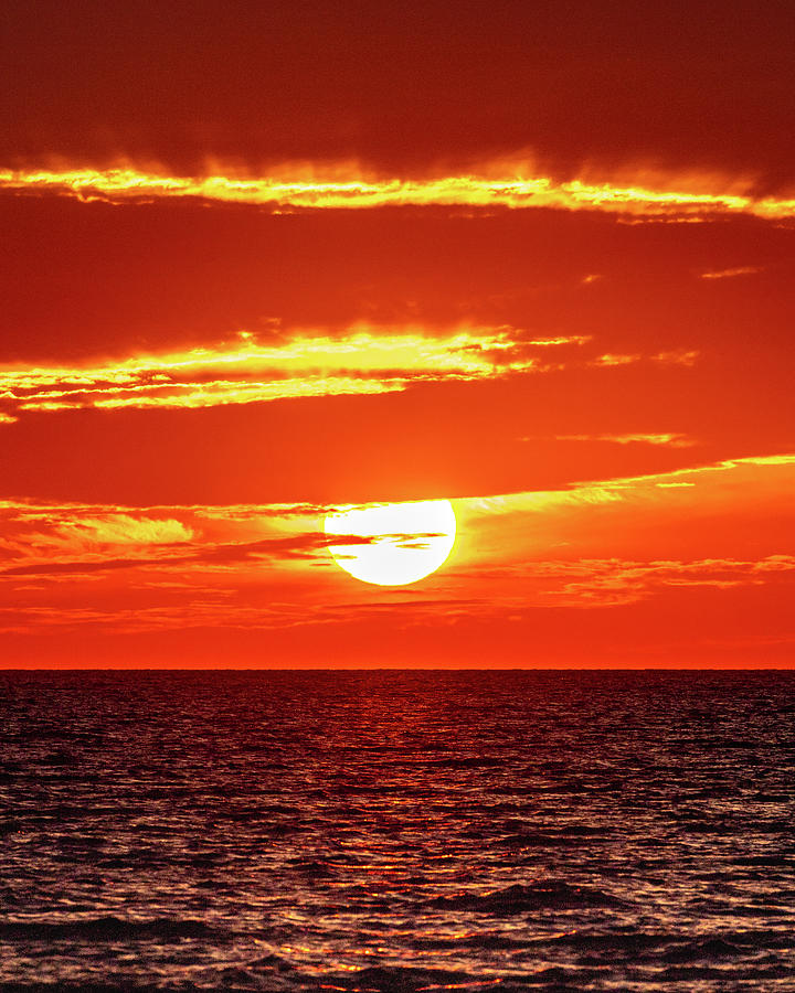 Sun Setting Along The Ocean's Horizon Blazing The Clouds With Fire ...