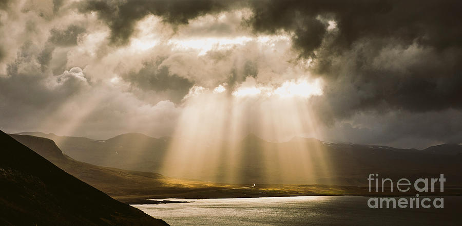 Sunbeams fall among the clouds in a lake between mountains. Photograph by Joaquin Corbalan