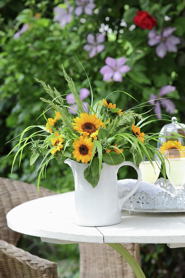 Sunflowers And Ornamental Grasses In Jug On Garden Table Photograph by Peter Raider