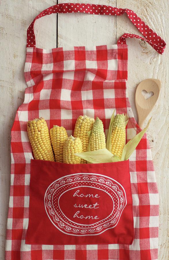 Sweetcorn In The Pocket Of A Red And White Checked Apron Photograph by Sylvia E.k Photography