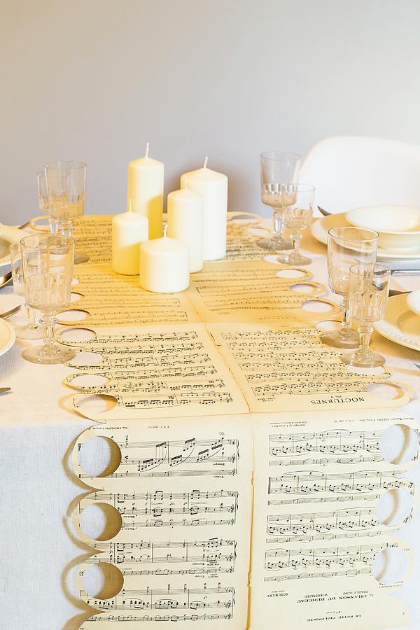Table Runner Hand-made From Sheet Music, White Pillar Candles And Crystal Glasses Photograph by Ivan Autet