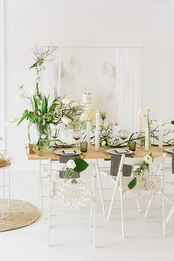 Table Set For Wedding With Vase Of Tulips, Dry Twigs And Pillar Candles In Front Of Wedding Cake On Sideboard Photograph by Katja Heil