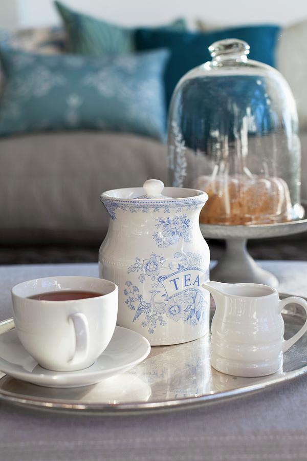 Teacup, Milk Jug And Tea Caddy On Silver Tray With Cake Under Glass Cover In Background Photograph by Great Stock!