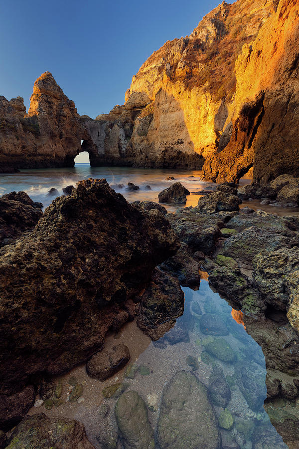The Algarve Rocks Radiating A Yellow Glow In The Morning Sunlight With Crystal-clear Water Of The Atlantic Ocean And A Clear Blue Sky, Algarve, Portugal Photograph by Tobias Richter