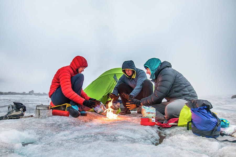 Mountain Photograph - Three Climbers Warm Their Hands Over A Fire While Camping On A Glacier by Cavan Images