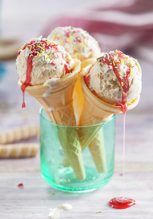 Three Cones Of Vanilla Ice Cream With Strawberry Sauce And Sugar Sprinkles In A Light Blue Glass Photograph by Stacy Grant