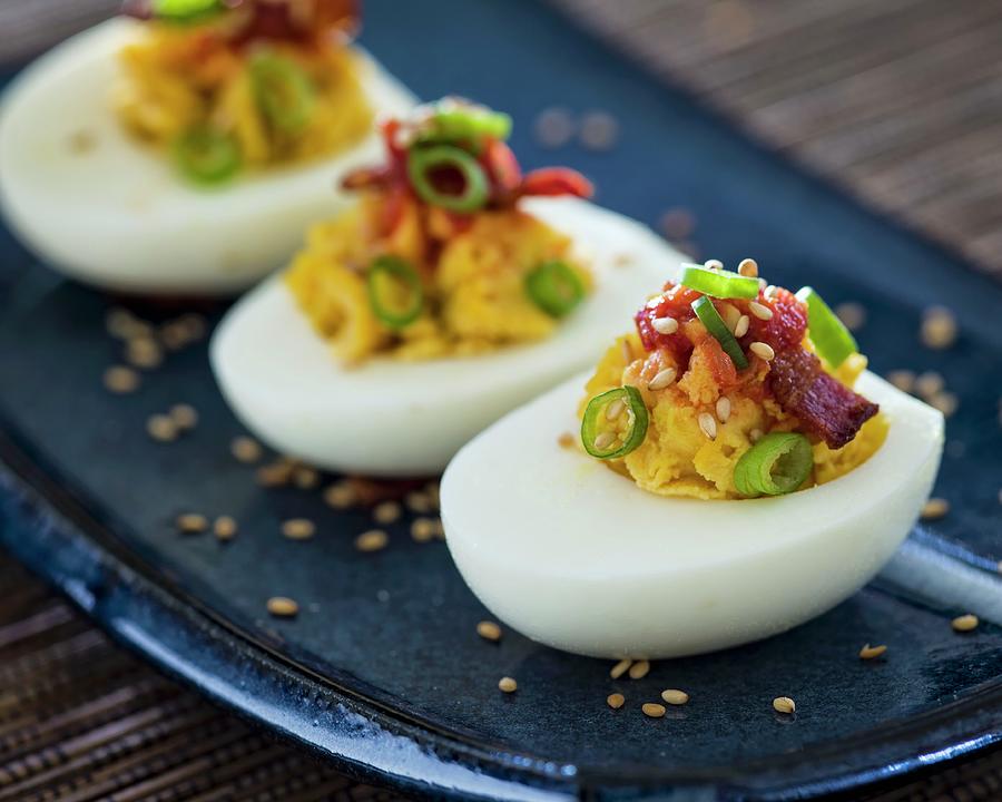 Three Deviled Egg Halves With Green Onions And Bacon Sitting On A Blue Asian-style Plate Photograph by Don Crossland