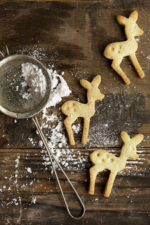 Three Festive Christmas Deer Shaped Cookie Biscuits On A Rustic Board With Icing Sugar In A Sifter Photograph by Stacy Grant