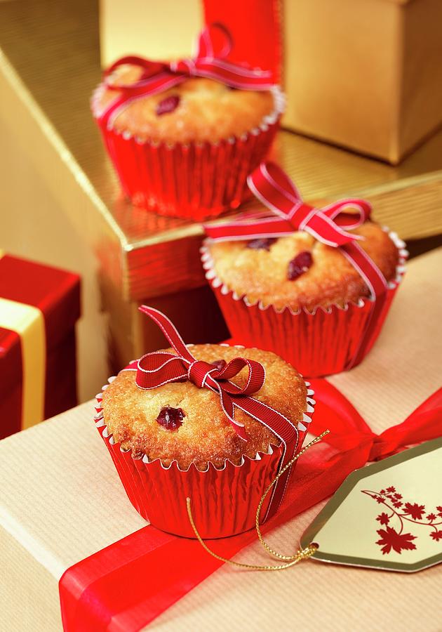 Three Festive Cranberry And Marzipan Muffins Tied With Ribbon Sitting On Wrapped Gifts In A Christmas Setting Photograph by Stuart Macgregor