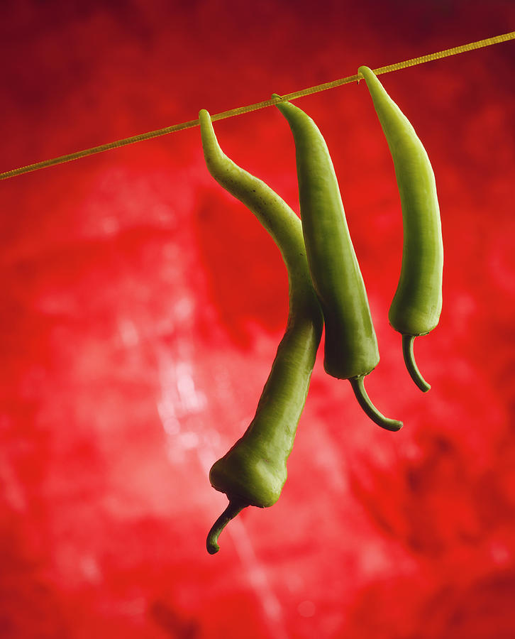 Three Green Chilli Peppers Hanging From A Line Against A Red Background Photograph by Michael Wissing