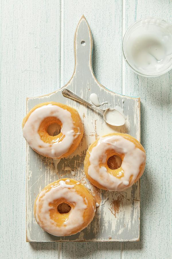 Three Iced Doughnuts On A Grey Wooden Chopping Board With A Spoon Photograph by Stacy Grant