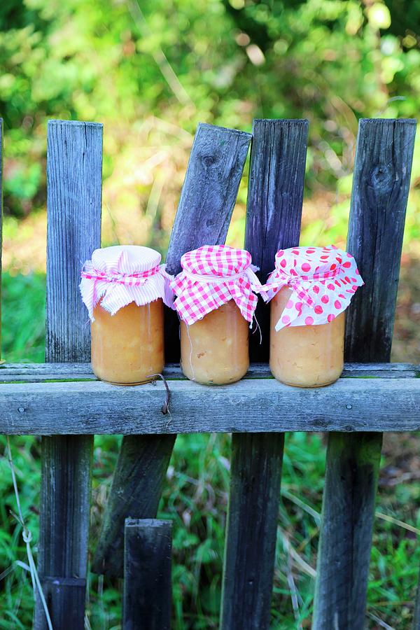 Three Jars Of Apple Sauce With Nostalgic Fabric Covers On Weathered Picket Fence In Late-summer Garden Photograph by Syl Loves