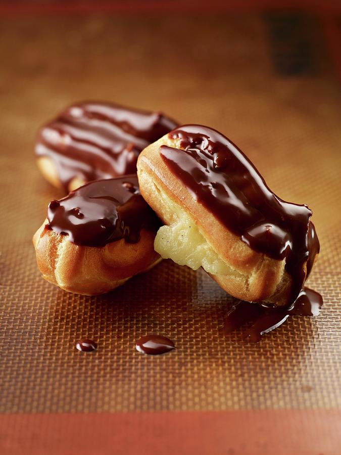 Three Mini Eclairs With Chocolate Glaze On A Baking Mat Photograph by Clinton Hussey