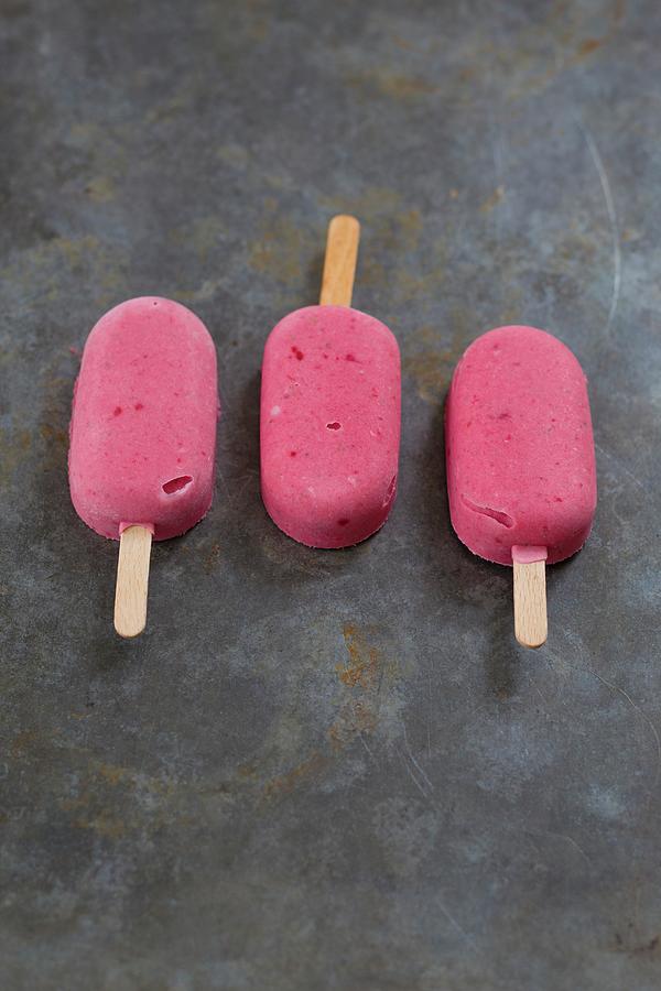 Three Raspberry Ice Lollies On A Grey Metal Background Photograph by Tina Engel