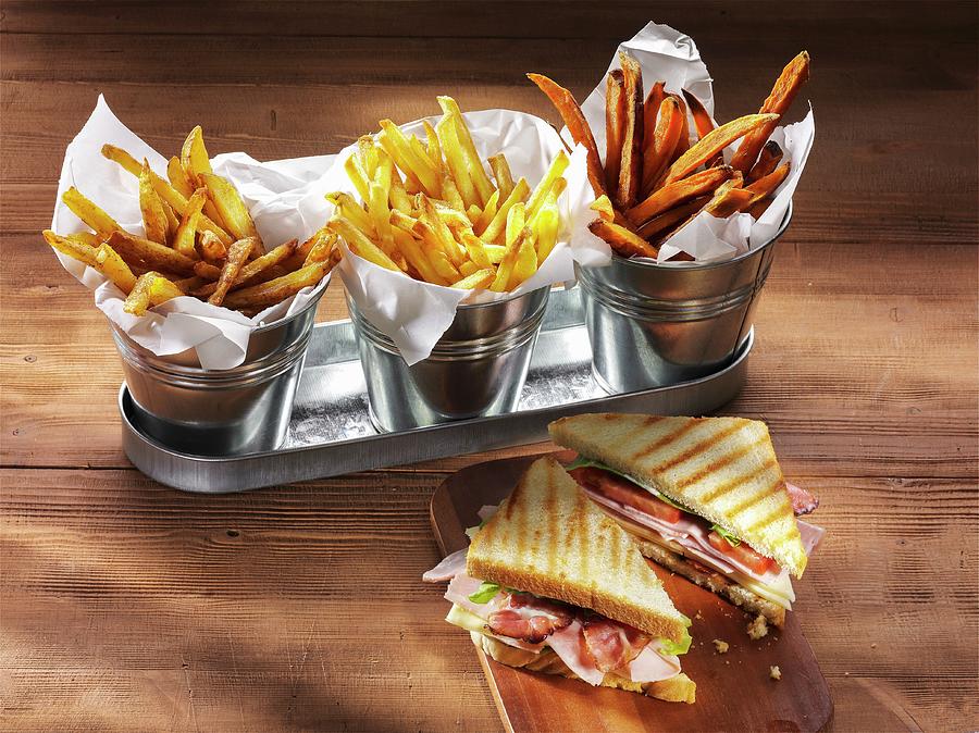 Three Types Of Chips And A Ham, Cheese, Tomato And Lettuce Sandwich On A Rustic Wooden Table Photograph by Christian Schuster