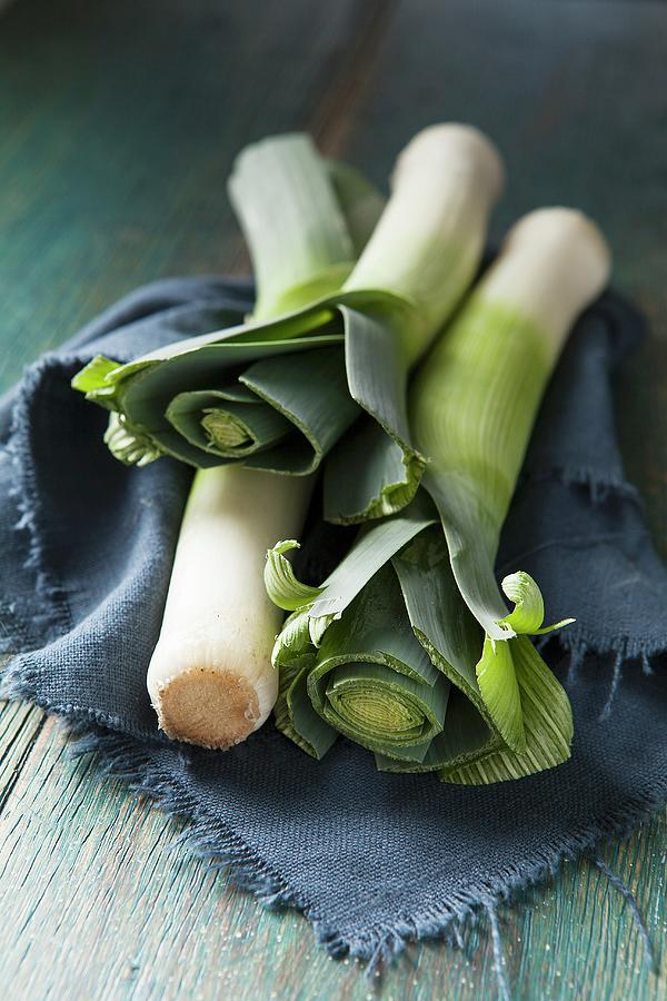 Three Whole Leeks On A Blue Cloth And Green Wooden Surface Photograph by Stacy Grant