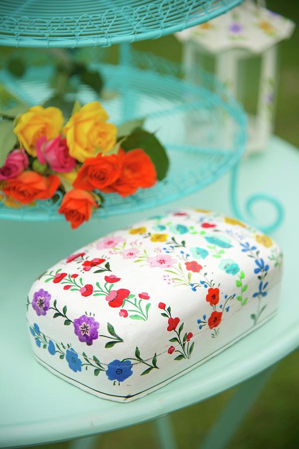 Tin With Floral Pattern And Flowers On Turquoise Cake Stand On Garden Table Photograph by Winfried Heinze