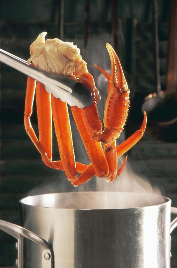 Tongs Holding Crab Legs Over A Steaming Stock Pot Photograph by Paul Poplis