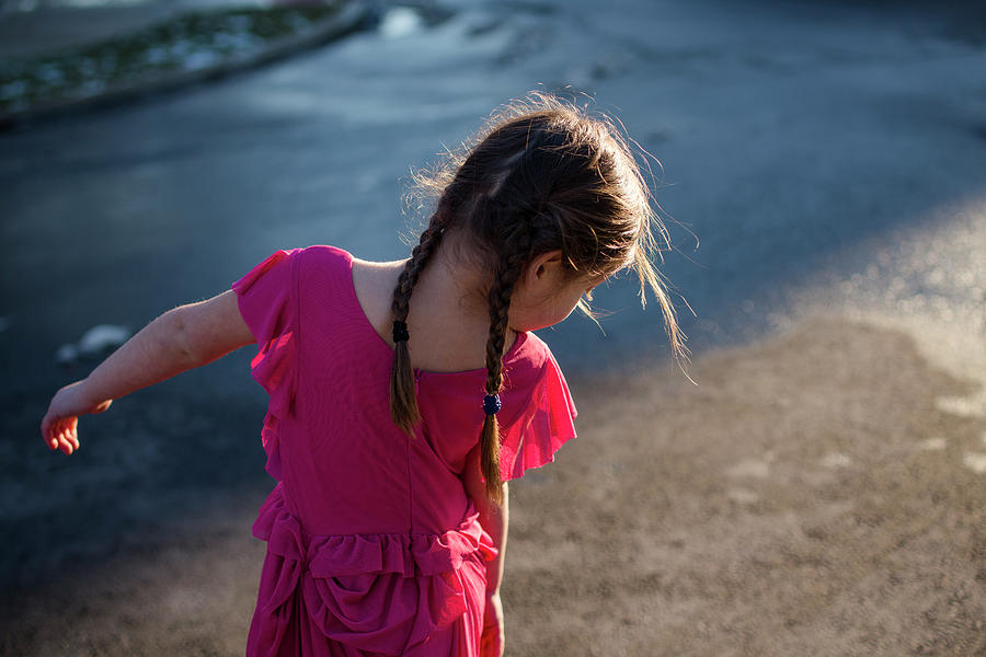 Top Half Of Little Girl With Long Braids Walking On A Street At Sunset 