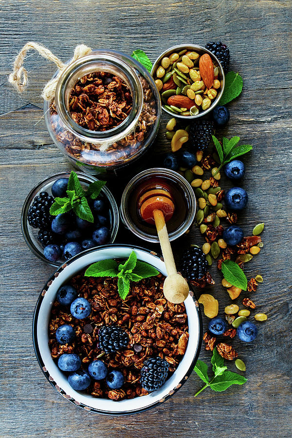 Fruit Photograph - Top View Of Chocolate Granola In Open Jar And Honey Served With Berries, Nuts And Fresh Mint For Tasty Breakfast On Rustin Wooden Table by Yuliya Gontar
