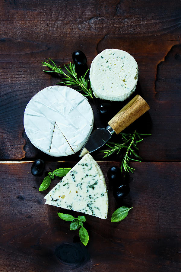 Top View Of Rustic Kitchen Table With Different Kinds Of Cheese, Olives, Basil And Rosemary On Dark Wooden Background Photograph by Yuliya Gontar