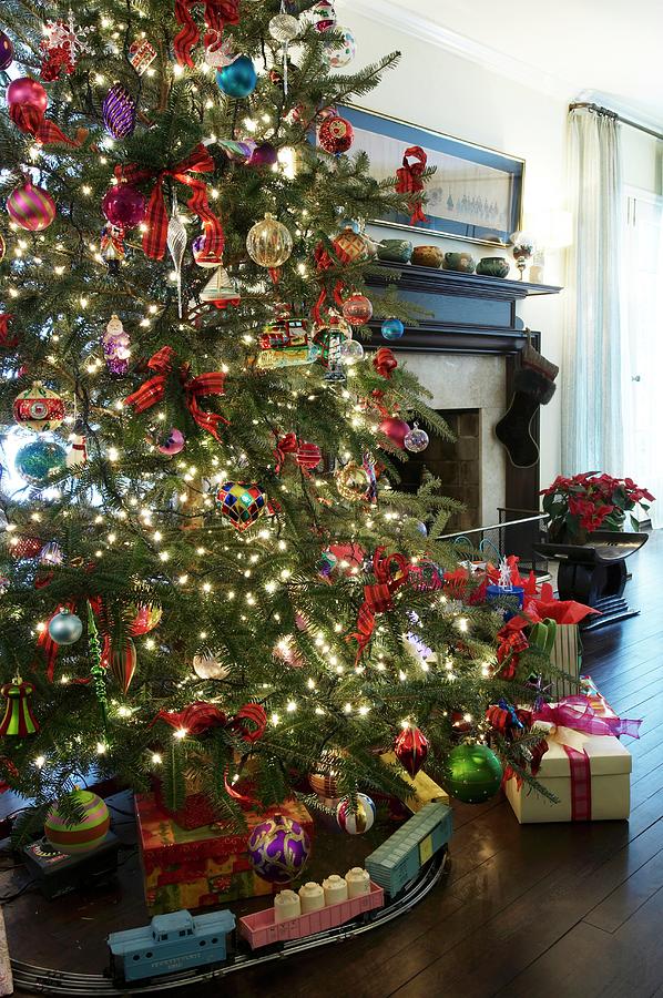 Toy Train Below Christmas Tree With Colourful Decorations And Sparkling Lights In Front Of Traditional Fireplace Photograph by Anastassios Mentis Photography