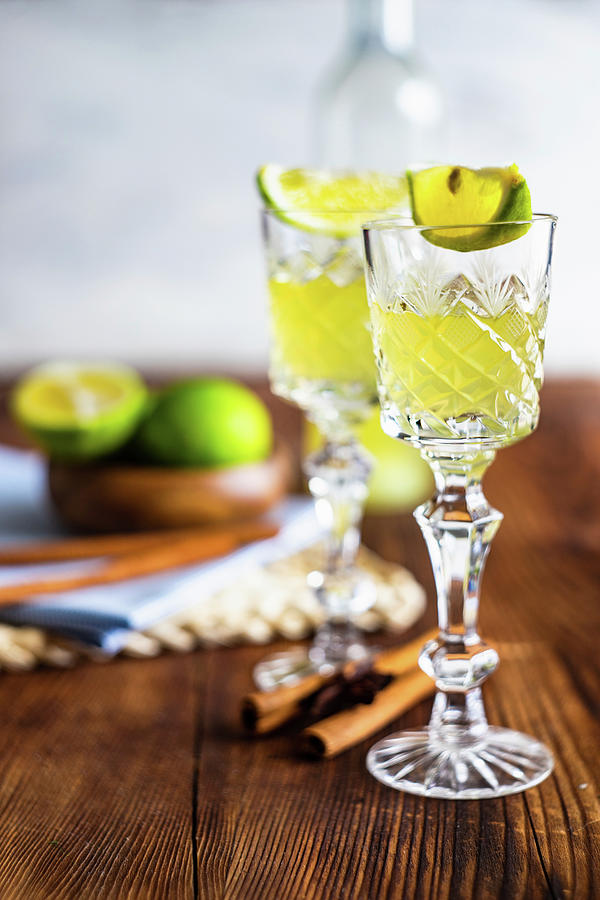 Traditional Italian Lemon Alcohol Drink Limoncello With Pieces Of Lemon And Rosemary Herb On Dark Wooden Table Photograph by Anna Bogush