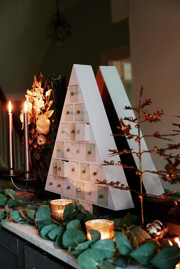 Triangular, Fir-tree-shaped Chest Of Tiny Drawers As Perpetual Advent Calendar Arranged On Mantelpiece With Plants And Candles Photograph by Catherine Gratwicke