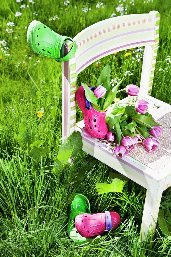 Tulips And Garden Clogs On Childs Chair In Tall Grass Photograph by Atelier Hmmerle