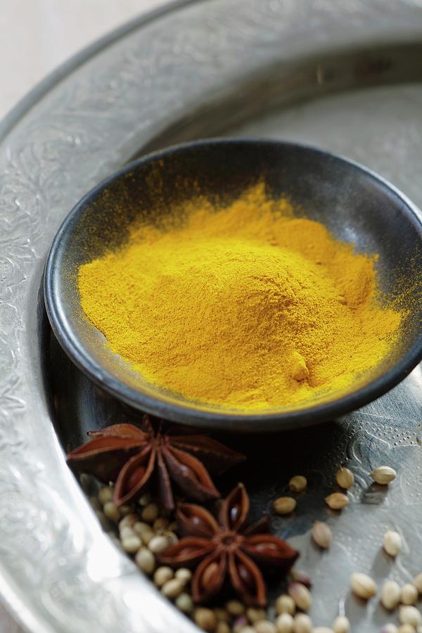 Turmeric Powder In A Black Bowl With Star Anise And Coriander On A Silver Plate Photograph by Victoria Firmston