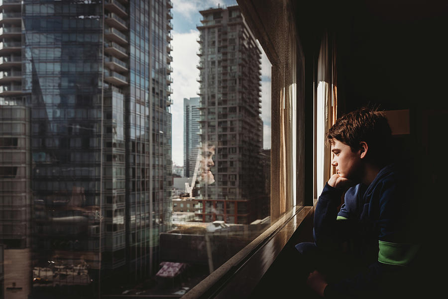 Architecture Photograph - Tween Boy Looking Out A Window At Tall Buildings Of The City Outside. by Cavan Images