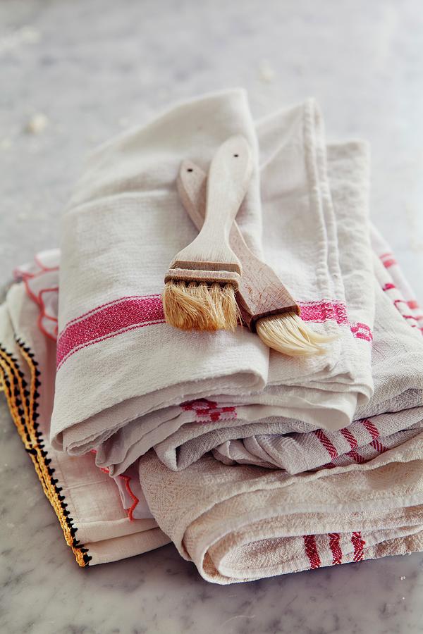 Two Baking Brushes On A Stack Of Tea Towels Photograph by Ulrika Ekblom
