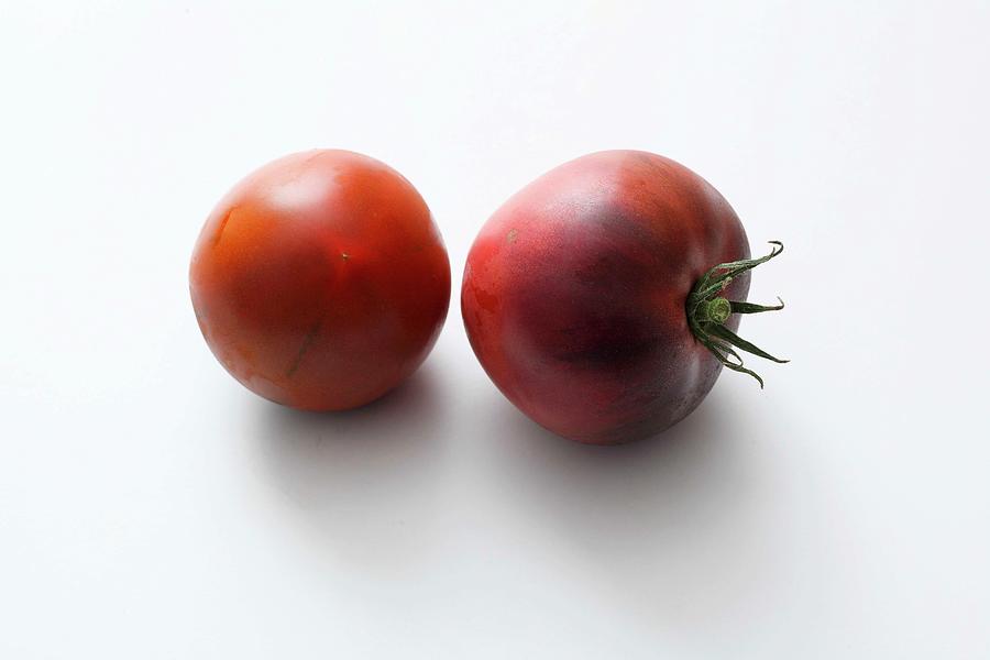 Two Black Tomatoes On A White Surface Photograph by Jalag / Mathias Neubauer